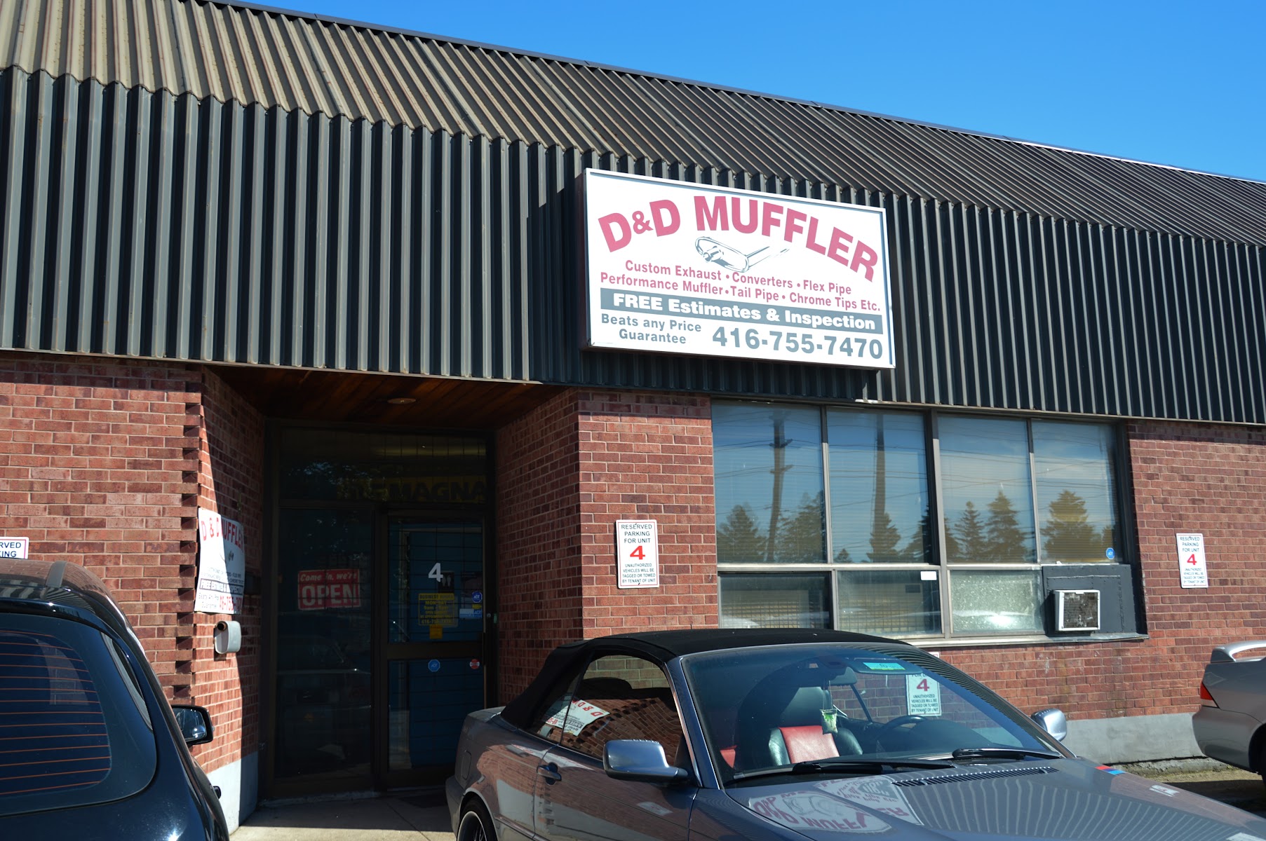 D&D Muffler shopfront with red and white sign, four reserved parking bays, and brick exterior at 15 Crockford Blvd, Scarborough